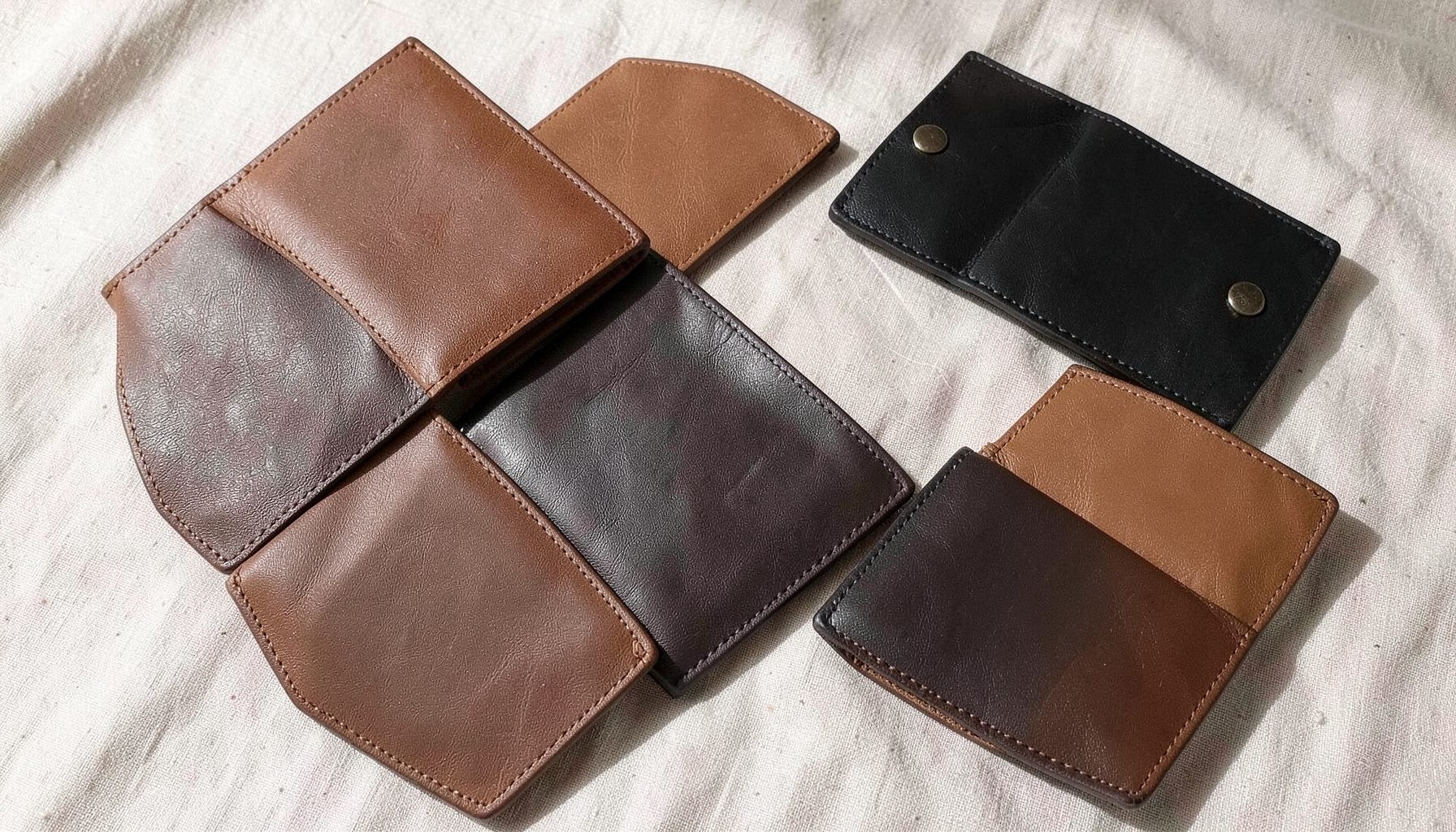 A flat-lay arrangement of slim vegan leather wallets and cardholders in warm brown and black tones, resting on a light linen surface with soft natural shadows.