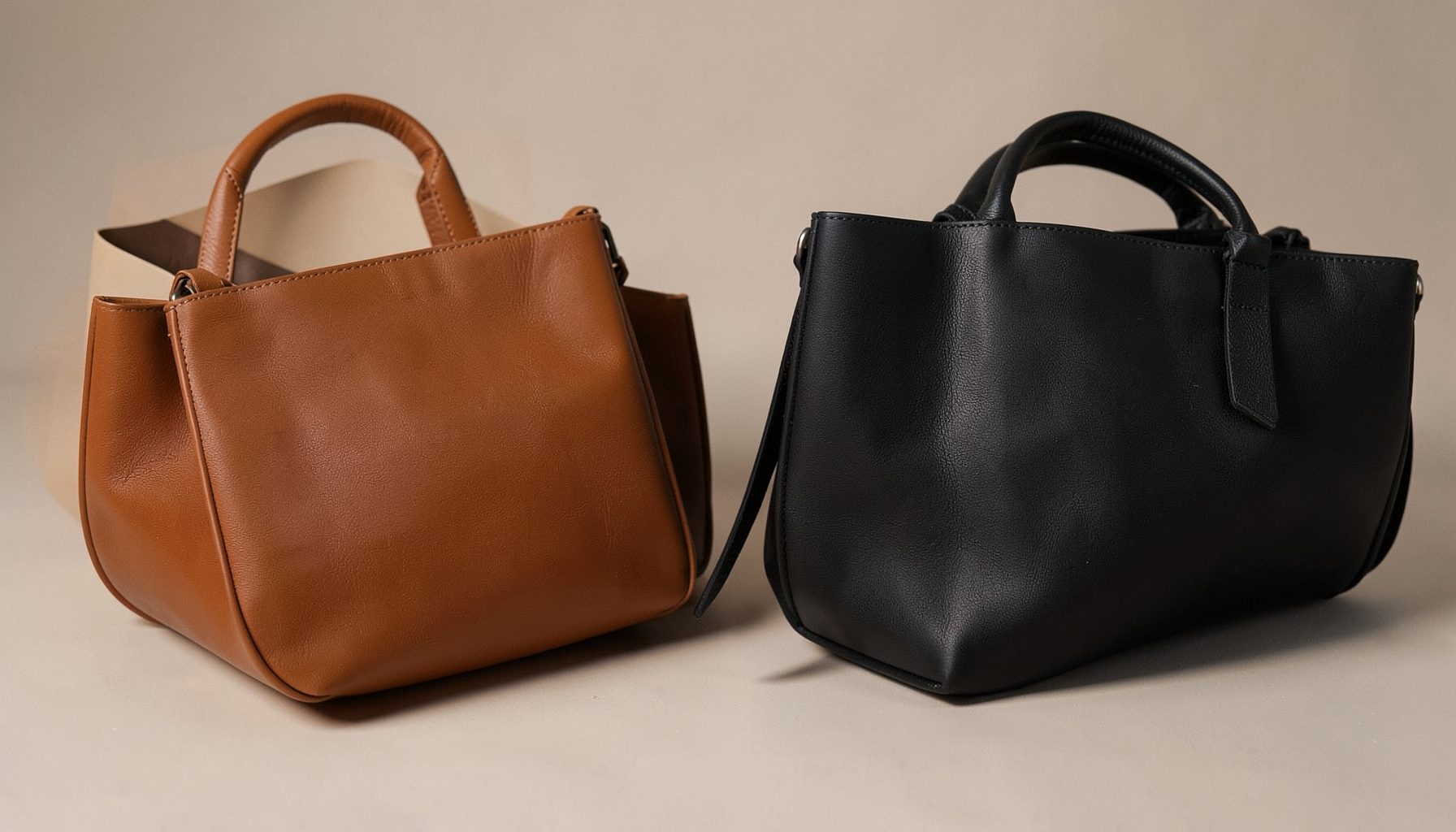 A softly lit arrangement of vegan leather bags in warm brown and black tones on a neutral surface, with gentle shadows and a clean modern feel