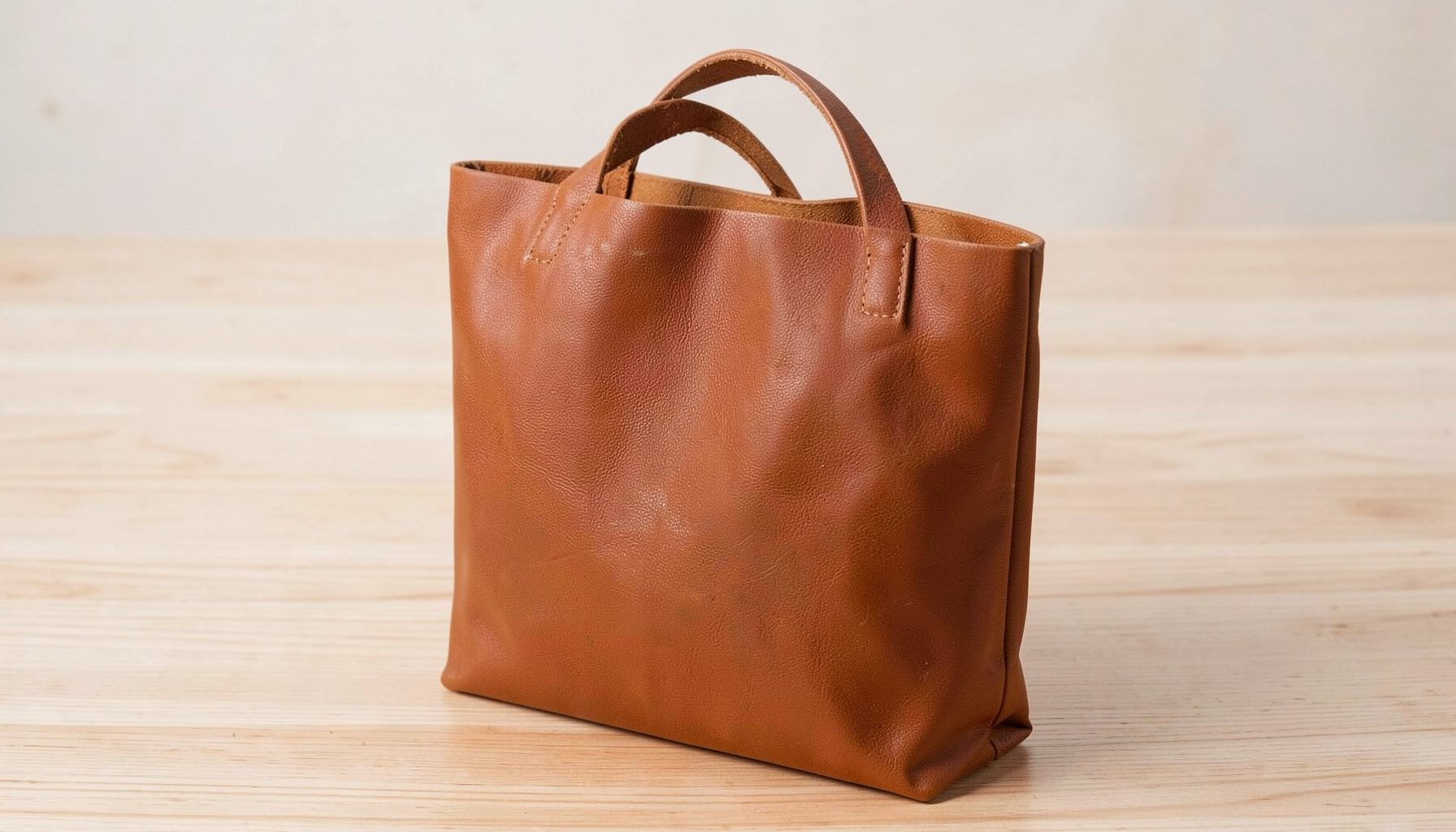 A warm brown vegan leather tote with subtle texture, placed on a light wooden surface