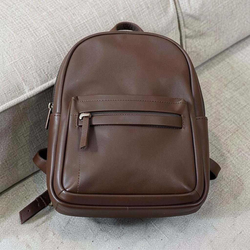 Classic structured vegan leather backpack in deep brown with clean stitching, resting on a textured fabric surface.