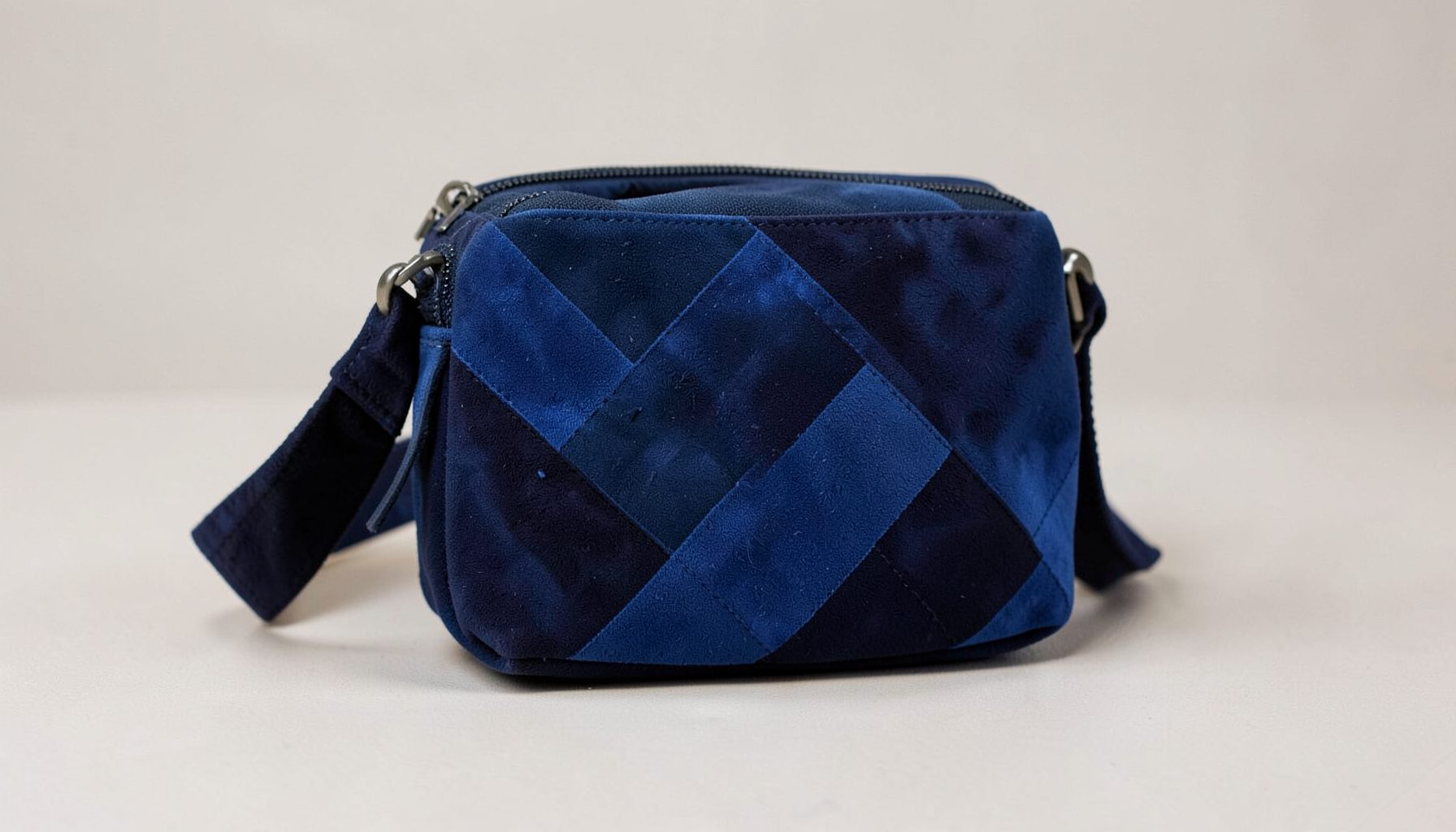 Deep navy and royal blue toned suede crossbody bag with a geometric pattern resting on a light neutral surface, evoking a sleek and sophisticated travel mood